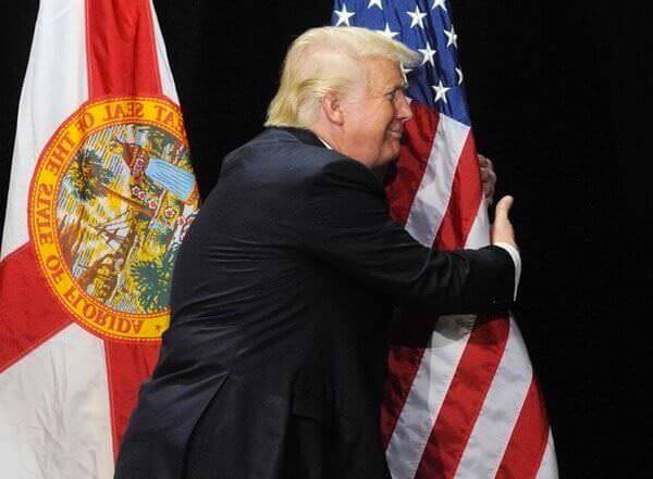 Trump hugging American Flag with weird smile on his face.